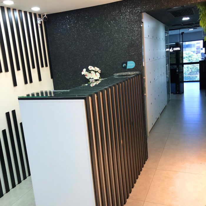 Na foto mostra uma recepção com bancada em ripado preto e branco, com paredes pretas com gliter e boa iluminação, com um corredor que dá acesso à copa, banheiros e salas privativas.